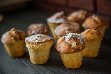 Fresh cooked cupcakes. Delicious homemade muffins with a pear. Cupcakes with a blue napkin on a dark black wooden table. Cupcakes, muffins sprinkled with powdered sugar on the background of a red bric