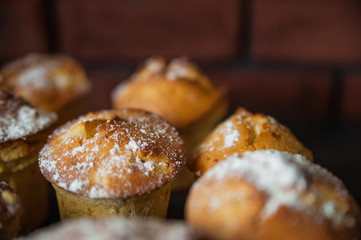 Fresh cooked cupcakes. Delicious homemade muffins with a pear. Cupcakes with a blue napkin on a dark black wooden table. Cupcakes, muffins sprinkled with powdered sugar on the background of a red bric
