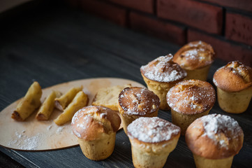 Fresh cooked cupcakes. Delicious homemade muffins with a pear. Cupcakes with a blue napkin on a dark black wooden table. Cupcakes, muffins sprinkled with powdered sugar on the background of a red bric