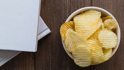 potato chips in a white bowl and book pile on wooden table, view from above