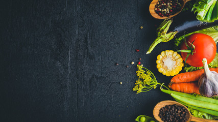 A large selection of raw fresh vegetables and spices. On a black wooden background. Top view. Free space for your text.