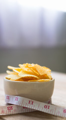 potato chips in a white bowl and measuring cable on wooden table