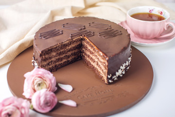 Delicious chocolate layered cake with nougat and sponge cake in the cut. Served flowers roses and pink Cup of tea