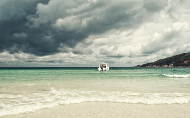 Exotic beautiful marine beach in Thailand with boat on blue water and stormy clouds sky