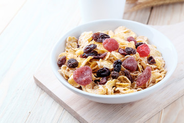 cornflakes and dry berry fruits in a white bowl on a wooden background.