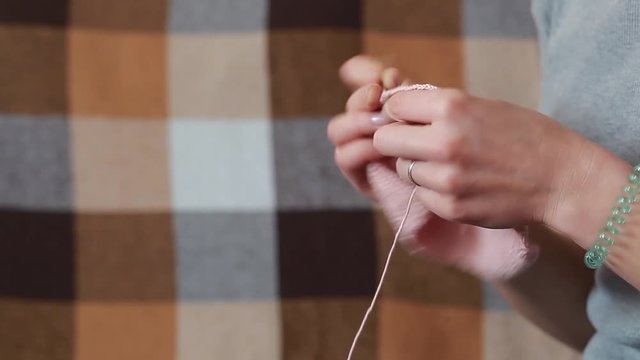 A young woman in a gray T-shirt knit a scarf crocheted with pink thread of natural wool, side view