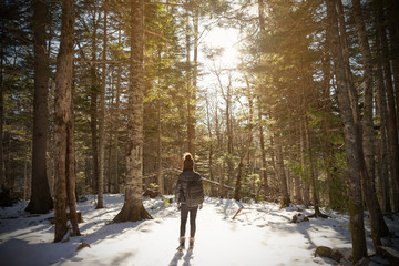 A young woman standing in the middle of a pine tree forest during a winter day in Akan, Hokkaido, Japan.