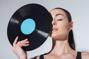 Close-up portrait of pretty brunette girl with closed eyes holding vinyl record isolated on grey