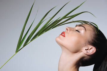 Fototapeta premium Close-up view of beautiful young woman with perfect skin holding green palm leaf