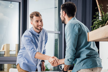 Fototapeta premium handsome smiling businessmen shaking hands at meeting in office