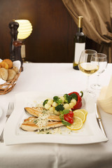 Hake fillet with grilled vegetables arranged on a plate, Wine bottle and wineglass in background, Traditional dish in elegant setting, Selective focus with soft light