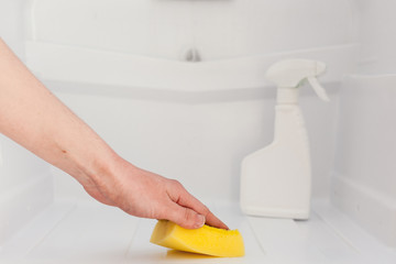Woman's hand cleaning white fridge with yellow sponge at kitchen.