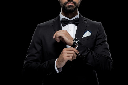 cropped view of businessman in bow tie and tuxedo with watch, isolated on black