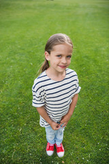 High angle view of adorable little girl standing on green grass and smiling at camera