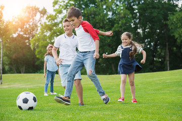 Cute happy multiethnic kids playing soccer with ball in park