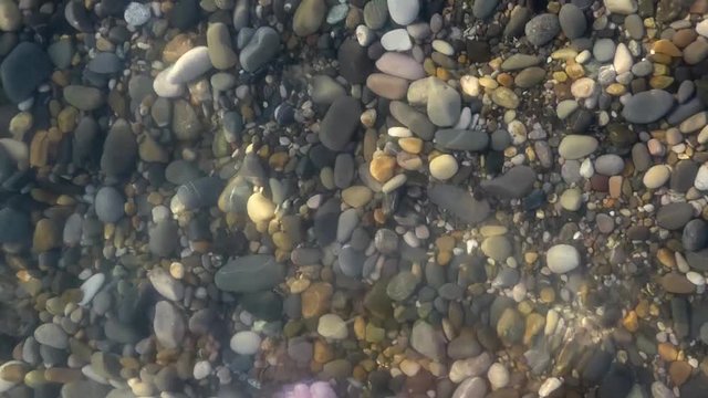Pure water surface above polished stones, closeup view. Underwater pebbles and sea waves. Sunny summer day. Natural background.