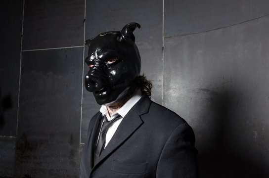 A corporate man in a dirty scruffy suit wearing a black pigs mask in a dark sinister background, photographed with moody cinematic lighting. evil dirty corporate pigs.