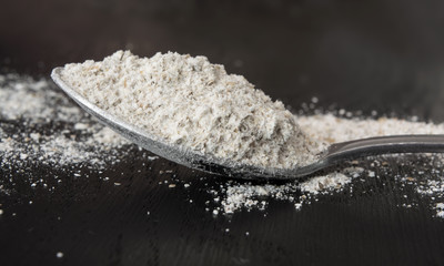 Spoonful of flour on black wooden background. Closeup