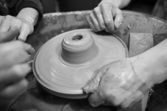 Hands working on a spinning pottery wheel, making pottery out of clay mud. close up photograph with a shallow depth of field.
