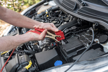 Hands of car mechanic using car battery jumper cable - obrazy, fototapety, plakaty
