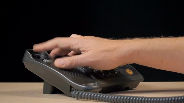 Wired phone in the office on the desk. A European man uses a telephone. Shooting in the studio on a black background. Close-up of the hands of a man.