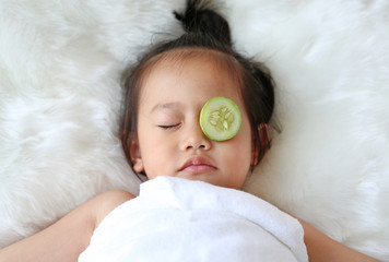 Cute little Child girl with a slice of cucumber in her eye, concept for skin care.