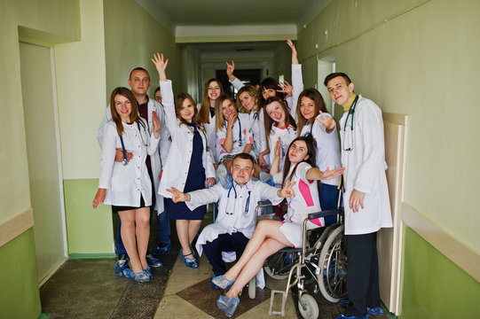 Crazy young doctors having fun by posing on a wheelchair in the hallway of hospital.