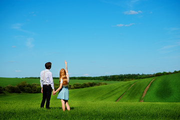 A young couple standing in the field, the girl shows her hand to the sky