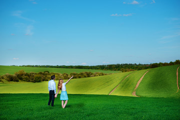 A young couple standing in the field, the girl shows her hand to the sky