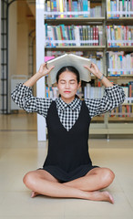 Young asian woman place a book on head in the library.