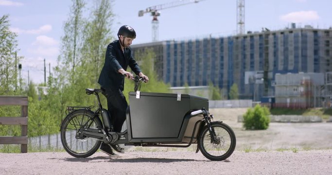 Young handsome architect arriving with his cargo bike at a construction site