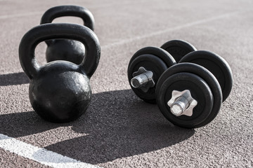 Obraz na płótnie Canvas Close up of a kettlebell and dumbells on a running track. Sport and fitness equipment.