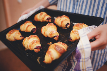 girl is holding a baking sheet with fresh croissants with a sweet, cherry filling.