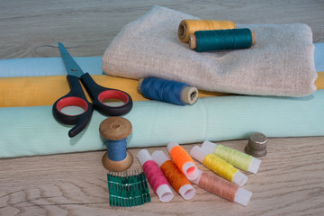 Sewing still life: colorful cloth. Sewing kit includes threads of different colors, thimble and other sewing accessories on wooden table