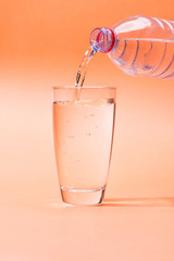 Pouring water from bottle to glass on orange background