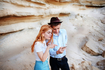 Attractive man and beautiful woman are looking at the screen of a smartphone on the background of a sand quarry