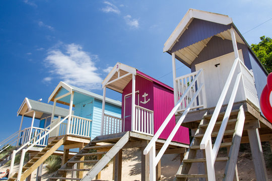 Rows of colourful wooden beach huts on a sandy beach in Norfolk, UK under a blue sky and summer sunshine.