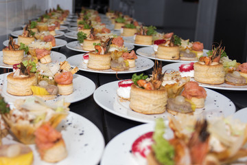 Many plates of appetizers being prepared in commercial kitchen, for an event