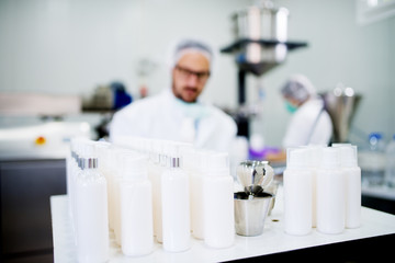 Young technologist making face care creams. Sitting in a cosmetic products factory working with laptop.