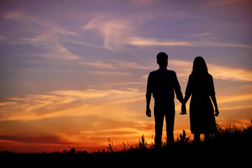 young couple is holding hands on a background sunset silhouette