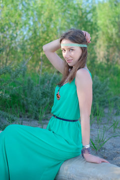 Beautiful girl hippie in a green dress sitting on a log