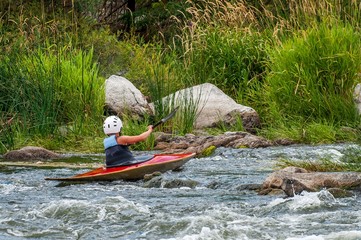 A teenager trains in the art of kayaking. Boat boats on rough river rapids. The child is skillfully engaged in rafting.