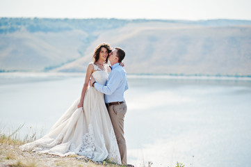 Pretty bride and groom kissing on the edge of rocky cliff with a stunning scenery on the background.