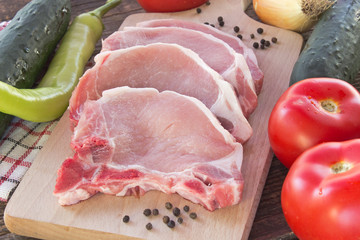 Raw pork chop meat with vegetables on cutting board
