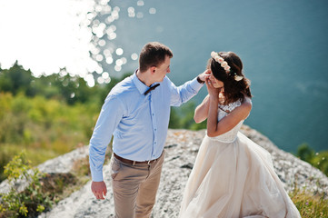 Fantastic wedding couple standing on the edge of rocky precipice with a perfect view of lake on the background.