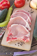 Raw pork chop meat with vegetables on wooden table