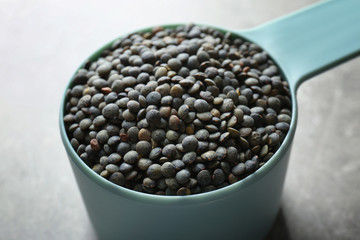 Measuring scoop with black lentils on light background