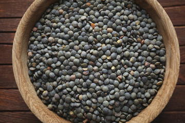 Bowl with black lentils on wooden background