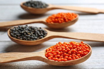 Spoons with red and black lentils on wooden background