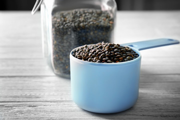 Fototapeta na wymiar Measuring scoop with black lentils on light background
